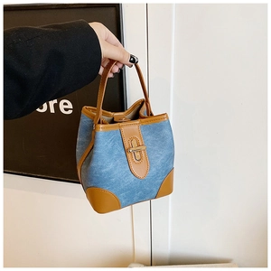 Detailed close-up of blue denim bucket bag with brown leather trim and metal swivel lock