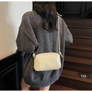Close-up of yellow polka dot baguette bag with B logo worn on grey knit sweater