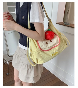 Detail of light yellow apple-shaped nylon shoulder bag with cute plush fruit pendant