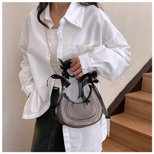 Detail of grey PVC crescent bag with black ribbon bows and golden chain strap for women