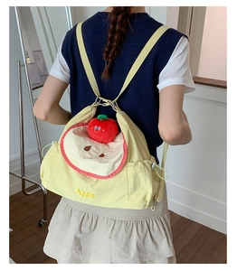 Detail showing the yellow cartoon apple shoulder bag with red plush charm and embroidery
