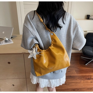 Detail showing tan pleated tote bag with silver star charm and leather label accent