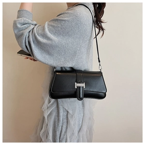Detail of matte black leather baguette bag featuring a silver H-shaped metal buckle clasp