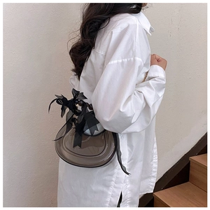 Detail view of a semi-transparent grey crescent bag with a black satin bow decoration