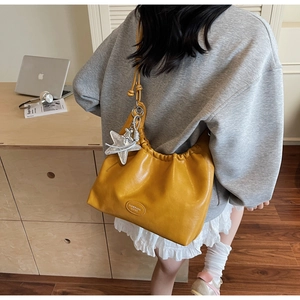 Detail of yellow pleated tote bag with silver star charm worn as a shoulder bag