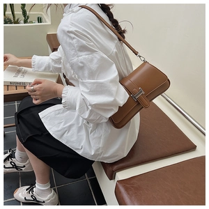 Brown leather baguette bag with silver metal buckle shown in a lifestyle street style shot