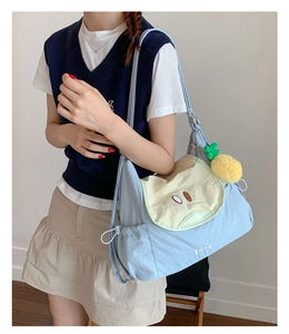 Detail view of light blue fruit canvas shoulder bag with apple flap and pineapple pendant