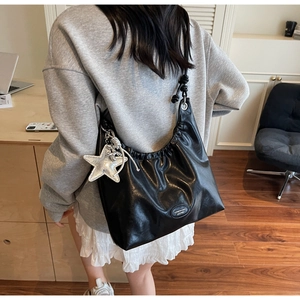 Detail of black pleated shoulder bag with metallic star pendant and silver logo patch