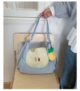 Detail view of light blue nylon crossbody bag with pineapple charm on wooden chair