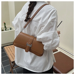 Detailed view of brown leather underarm bag with silver H-shaped buckle on a white shirt