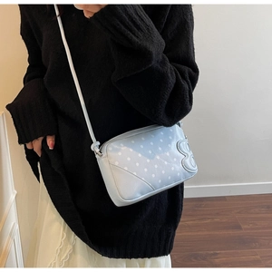 Detail shot of light blue polka dot crossbody bag with B-shaped charm and white strap
