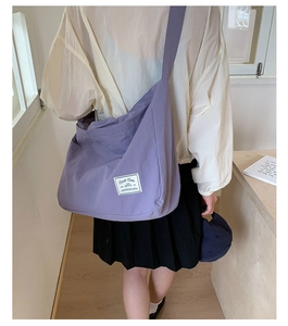Detail of a large purple canvas tote bag with white logo patch and wide shoulder strap
