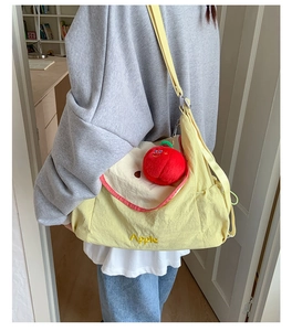 Detail of yellow canvas crossbody bag featuring Apple embroidery and red plush charm