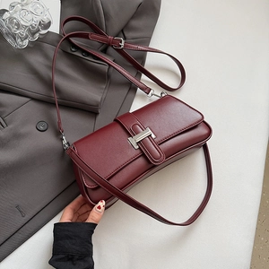Detail of burgundy leather baguette bag with silver buckle on grey suit background