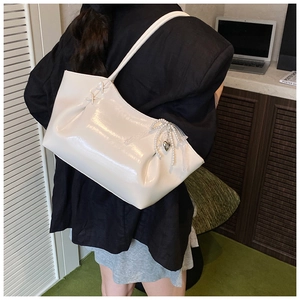 Détail du sac cabas en cuir verni blanc avec nœud en ruban et breloques perles