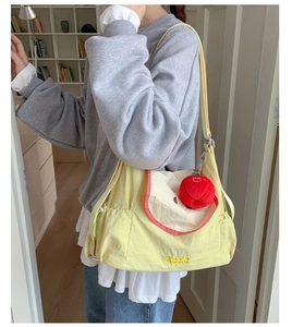 Detail of yellow canvas shoulder bag featuring red apple plush toy and Apple embroidery
