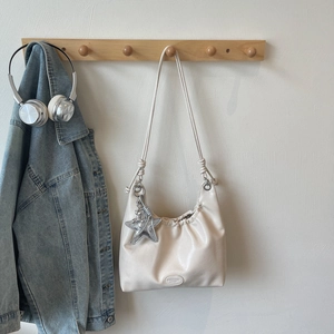 Detail of a creamy white pleated tote bag with a silver starfish pendant and slim straps