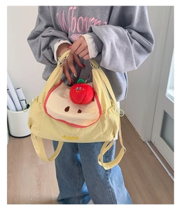 Detail of light yellow nylon tote bag with red apple plush charm and apple patch embroidery
