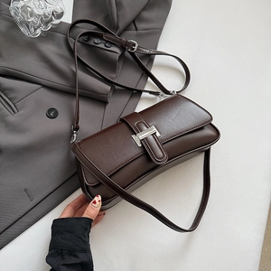 Detail of dark brown glossy leather baguette bag with silver metal buckle on a blazer