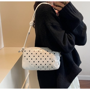 Detailed close-up of white polka dot shoulder bag with B-shaped charm and strap knot