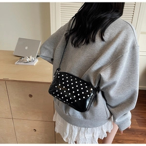 Close-up of a black and white polka dot crossbody bag worn by a model in a modern office