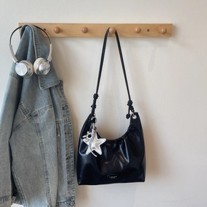 Close-up of black glossy leather tote bag with pleated detail and silver star charm