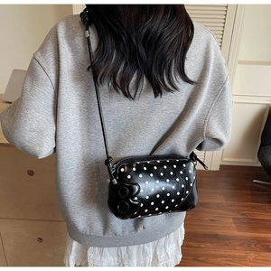 Detailed view of black polka dot shoulder bag with embossed B logo on grey sweater