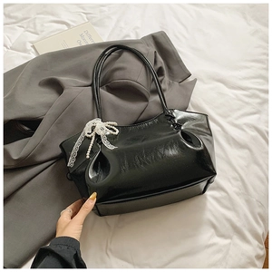 Détail du sac en cuir verni noir avec nœud en dentelle blanche et pendentifs en perles