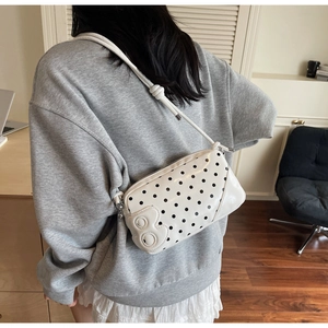 Close-up of white leather crossbody bag with black polka dots and 3D B-shaped patch