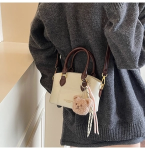 Detailaufnahme der cremefarbenen Mini-Handtasche mit braunen Griffen und Teddybär-Anhänger