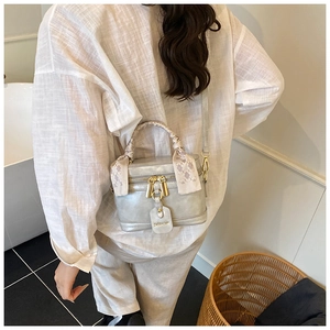 Close-up of a silver bucket bag with silk scarf handle and golden double zippers