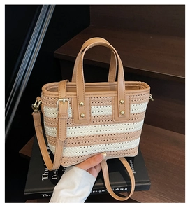Detail of striped woven straw bucket bag with leather handles and gold rivet accents