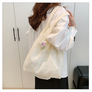 Close-up of cream lace tote bag with floral embroidery and plush flower charm on shoulder