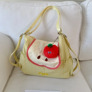 Close-up of cute yellow apple-themed crossbody bag with red plush pendant and embroidery