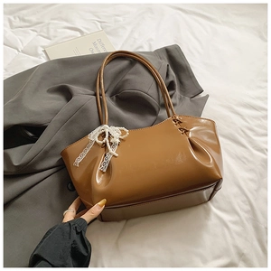 Détail du sac fourre-tout en cuir verni caramel avec nœud en dentelle et chaîne en perles