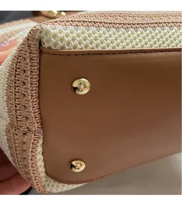 Detail of woven straw bucket bag showing brown leather base with gold protective metal studs