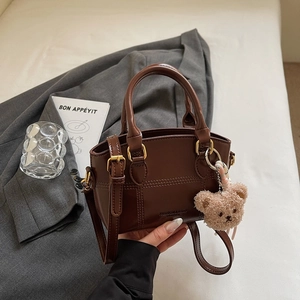 Detailansicht der braunen Ledertasche mit feinen Nähten und süßem Bärenanhänger