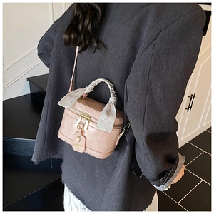 Pink bucket bag with silk scarf handle worn by model against a modern staircase