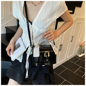 Detail of black glossy bucket bag featuring a silk scarf handle and gold double locks