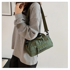 Détail d'un sac cylindrique en toile vert foncé avec bandoulière réglable et logo