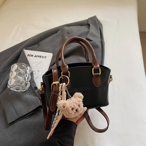 Detail einer schicken Kontrast-Handtasche mit Plüschbär-Anhänger und gestreiftem Schal