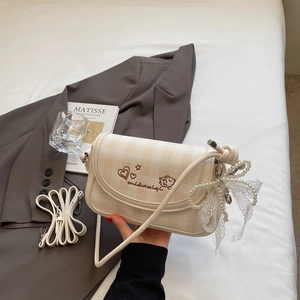 Detailed view of cream checkered shoulder bag with heart embroidery and pearl bow charm