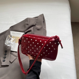 Detail of red polka dot shoulder bag featuring a stylish 3D bow accent and glossy finish