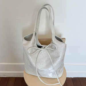 White faux leather tote bag featuring silver textures, studs and a large bow detail