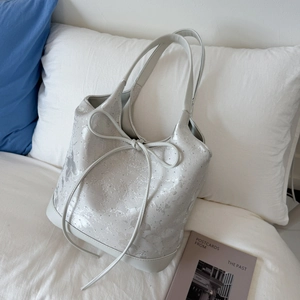 Detail of silver sequined tote bag with delicate bow knot on soft bedding background