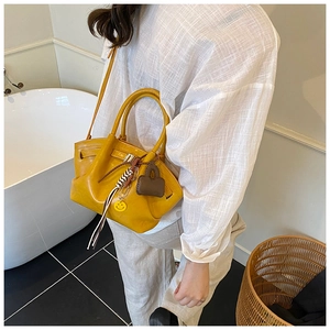 Detail of yellow dumpling tote bag with a smiley charm on a crossbody shoulder strap