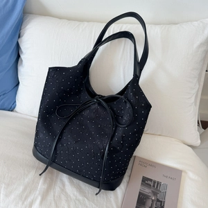 Detail of black polka dot tote bag with leather trim and bow tie on a cozy bed