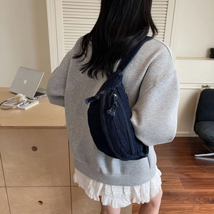 Detailed view of dark blue denim sling bag with white contrast stitching and silver zippers