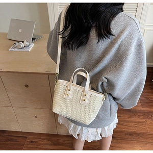 Close-up of woven bucket bag featuring white leather handles and gold metal hardware detail