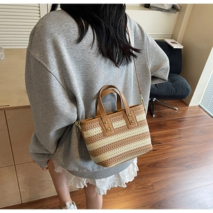 Close-up of woven straw bucket bag with brown leather handles and striped texture